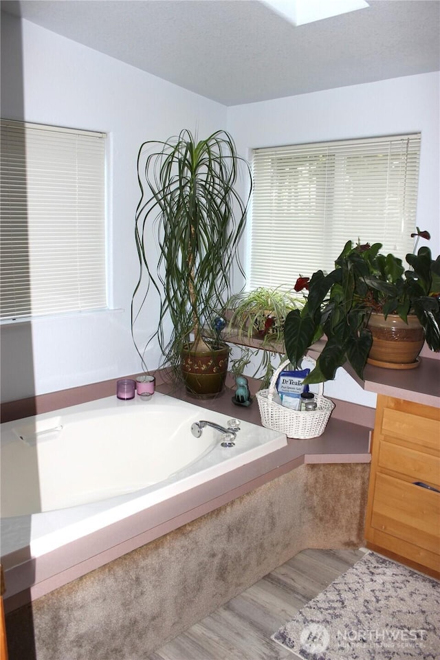 full bathroom featuring a skylight, a garden tub, and wood finished floors