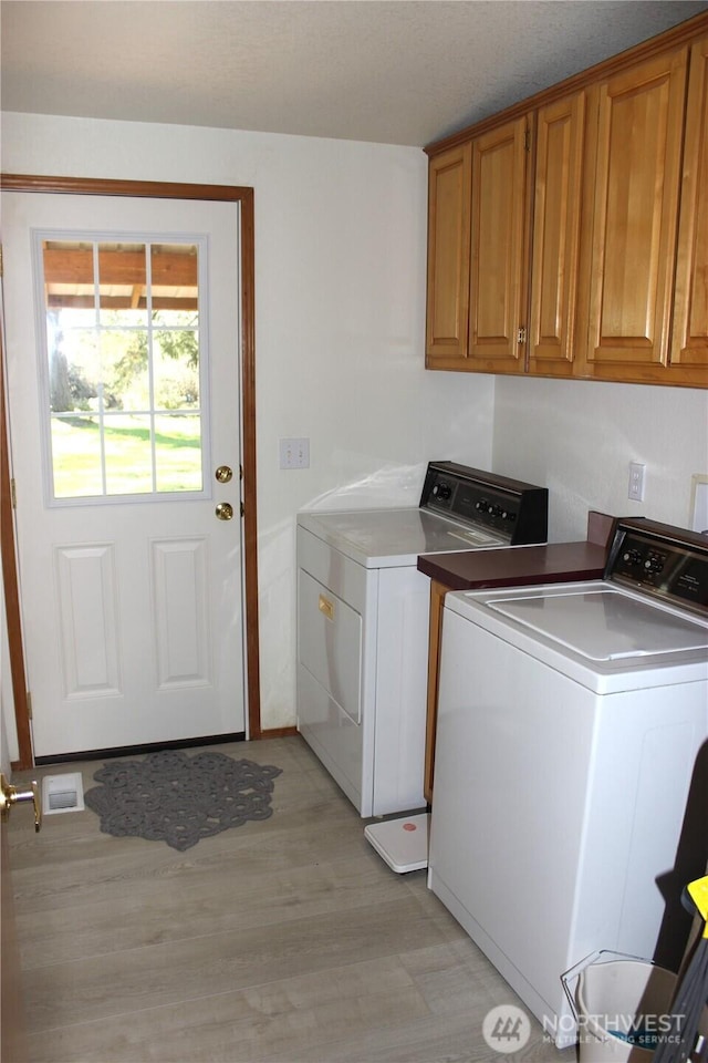 laundry room featuring light wood-type flooring, cabinet space, visible vents, and washing machine and clothes dryer