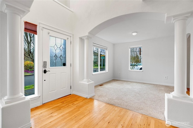 entryway featuring arched walkways, light wood-style flooring, baseboards, and decorative columns