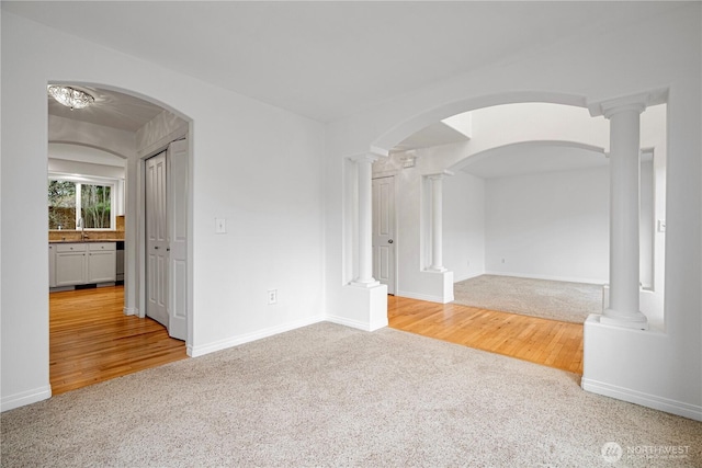 spare room with light wood finished floors, a sink, light colored carpet, and decorative columns