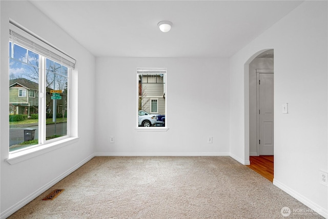 carpeted empty room with visible vents, arched walkways, and baseboards