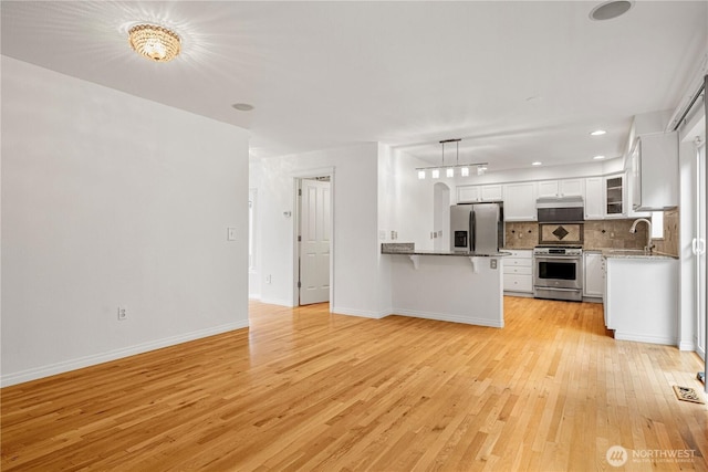 kitchen with a peninsula, light wood-style flooring, appliances with stainless steel finishes, a kitchen breakfast bar, and backsplash