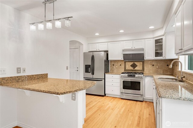 kitchen featuring light stone countertops, a kitchen bar, appliances with stainless steel finishes, a peninsula, and a sink