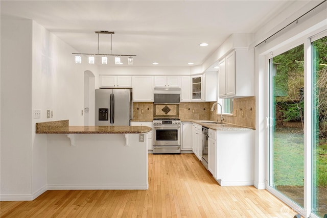 kitchen with a sink, dark stone countertops, tasteful backsplash, stainless steel appliances, and a peninsula