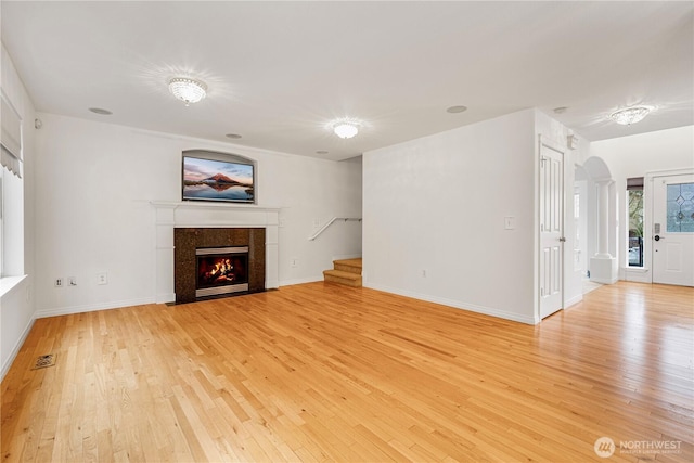 unfurnished living room with stairway, visible vents, arched walkways, a high end fireplace, and light wood-type flooring