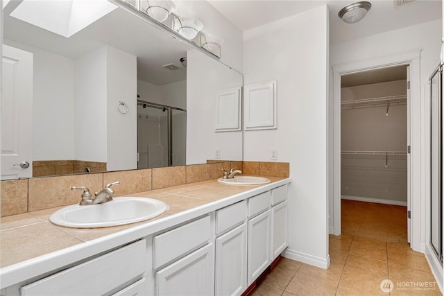 bathroom featuring tile patterned flooring, a shower stall, a skylight, and a sink