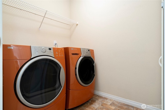 washroom featuring stone finish flooring, baseboards, laundry area, and washing machine and clothes dryer