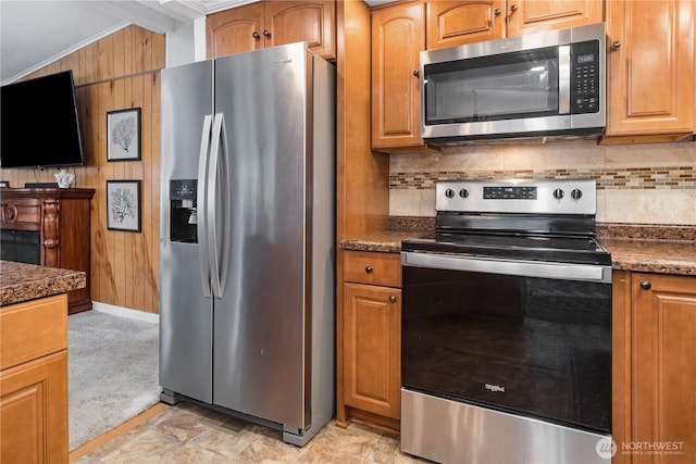 kitchen with decorative backsplash, light colored carpet, stainless steel appliances, and wooden walls