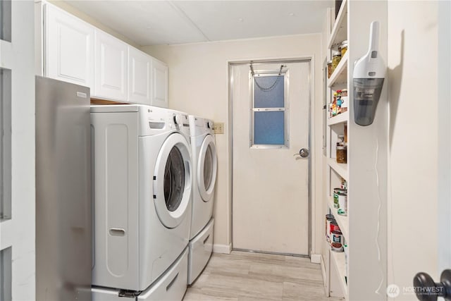 clothes washing area featuring washer and dryer, cabinet space, and light wood-style floors