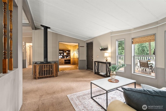 carpeted living room featuring a wainscoted wall, lofted ceiling, and a wood stove