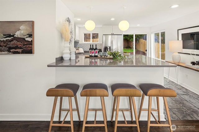 kitchen featuring a kitchen breakfast bar, tasteful backsplash, a peninsula, and stainless steel refrigerator with ice dispenser