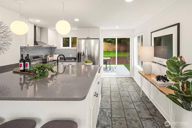 kitchen featuring backsplash, pendant lighting, stainless steel fridge, white cabinetry, and wall chimney exhaust hood