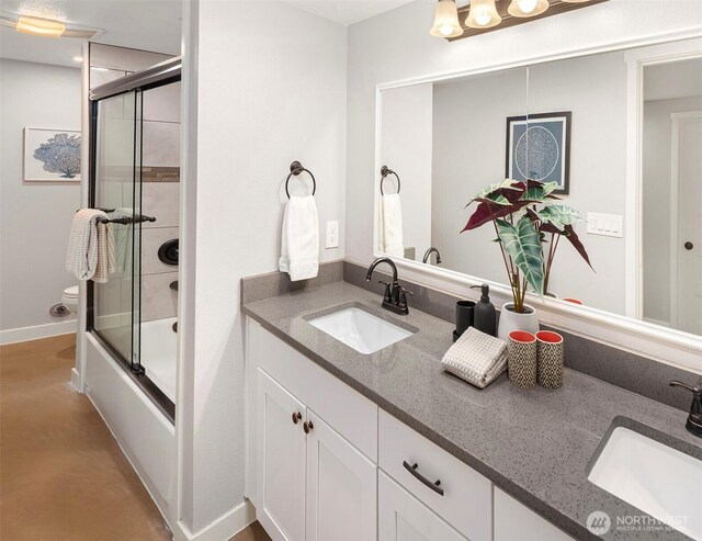 bathroom with a sink, enclosed tub / shower combo, toilet, and double vanity