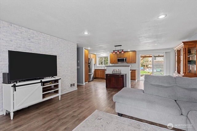 living room featuring dark wood-type flooring, plenty of natural light, visible vents, and a textured ceiling