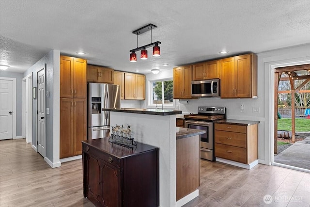 kitchen with dark countertops, appliances with stainless steel finishes, a center island, and light wood finished floors