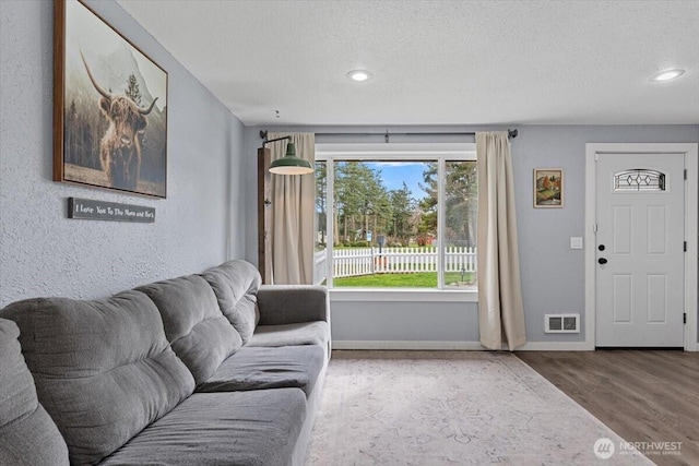 living room featuring visible vents, a textured ceiling, baseboards, and wood finished floors