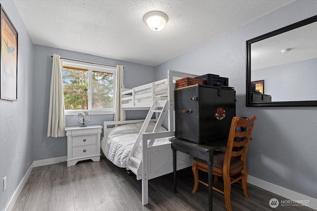 bedroom featuring baseboards, a textured ceiling, wood finished floors, and a textured wall