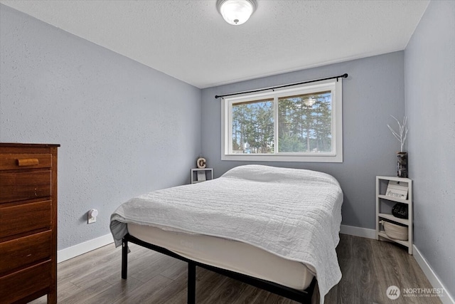 bedroom with wood finished floors, baseboards, a textured wall, and a textured ceiling