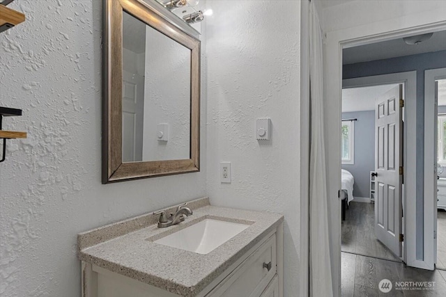 bathroom with vanity, wood finished floors, baseboards, a textured wall, and connected bathroom