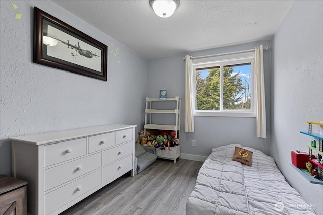 bedroom with baseboards, a textured ceiling, light wood-style floors, and a textured wall