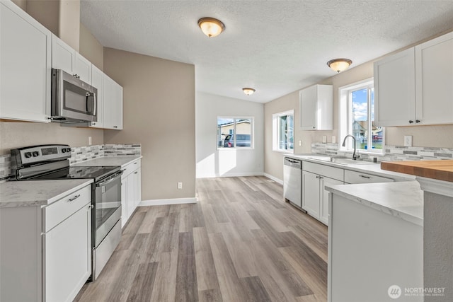 kitchen with a sink, appliances with stainless steel finishes, light wood-style flooring, and white cabinetry