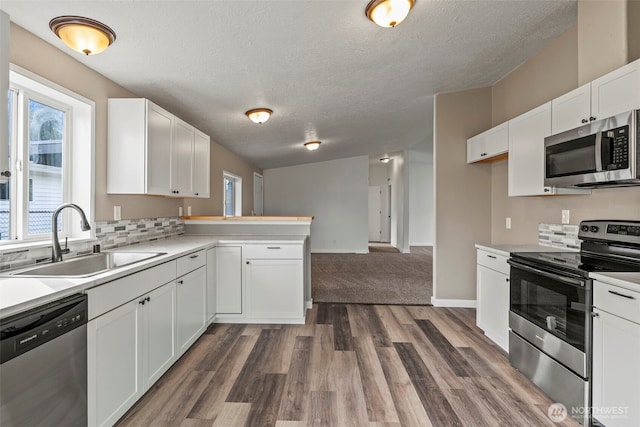 kitchen featuring light countertops, appliances with stainless steel finishes, a peninsula, white cabinetry, and a sink