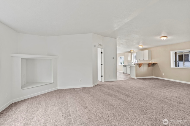 unfurnished living room with baseboards, light colored carpet, and a textured ceiling