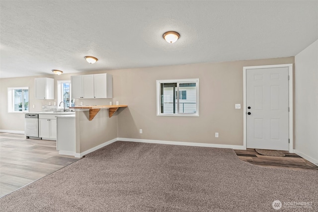 kitchen with a kitchen bar, light carpet, a peninsula, white cabinets, and stainless steel dishwasher