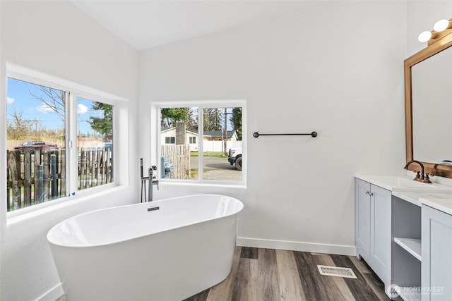 bathroom with vanity, wood finished floors, visible vents, baseboards, and a freestanding tub