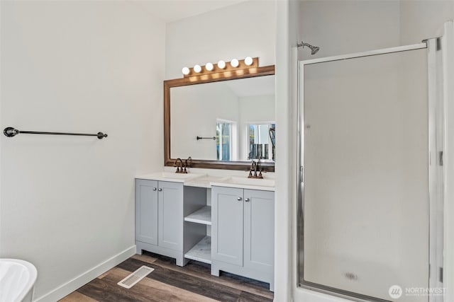 full bath featuring visible vents, a sink, wood finished floors, a shower stall, and double vanity