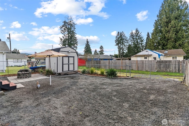 view of yard with an outbuilding, a storage unit, a fenced backyard, and a fire pit