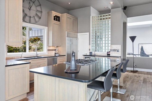 kitchen with a kitchen island, a sink, appliances with stainless steel finishes, dark countertops, and a kitchen breakfast bar