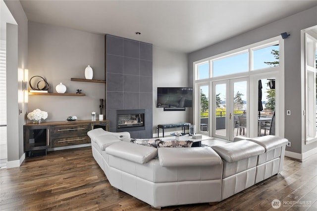 living room featuring dark wood-style floors, a tiled fireplace, french doors, and baseboards