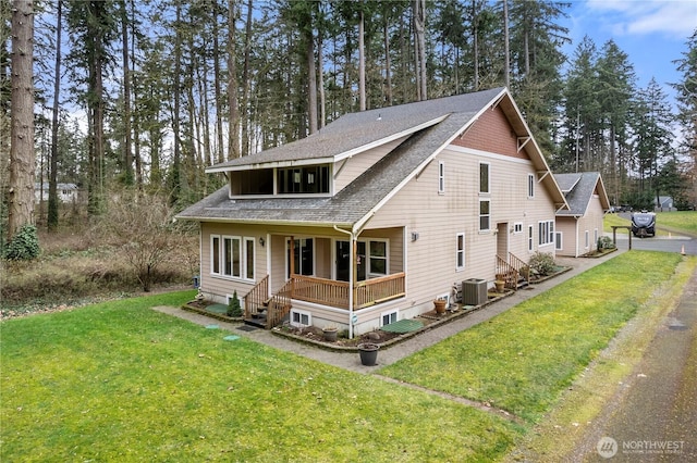 view of front of house with central air condition unit, roof with shingles, covered porch, and a front yard