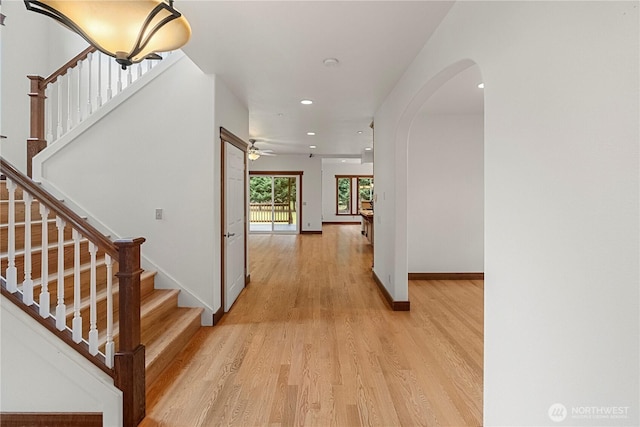 hallway featuring stairs, light wood-style flooring, baseboards, and arched walkways