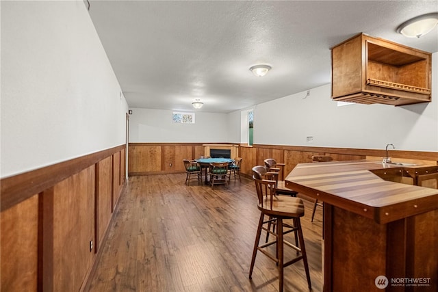 kitchen with a wainscoted wall, brown cabinets, a sink, open shelves, and wood finished floors