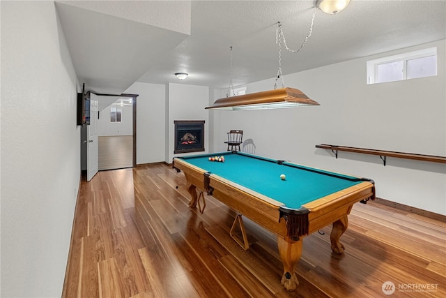 rec room featuring a textured ceiling, wood finished floors, a lit fireplace, pool table, and baseboards