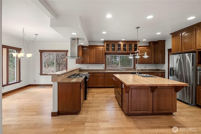 kitchen featuring butcher block countertops, a peninsula, exhaust hood, stainless steel appliances, and a sink