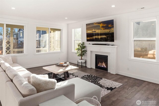 living area with recessed lighting, baseboards, a glass covered fireplace, and wood finished floors