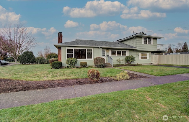 view of front of house with a chimney, a front yard, and fence