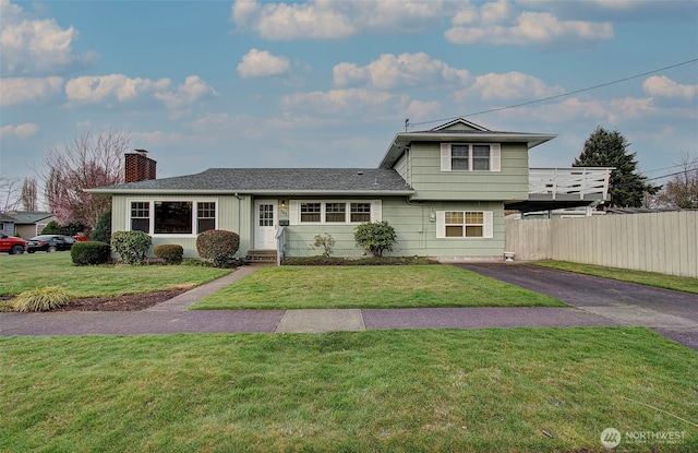 split level home with aphalt driveway, fence, a front yard, and a chimney