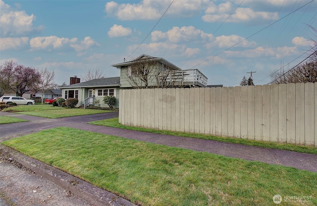 view of side of home with a lawn, fence, and a chimney