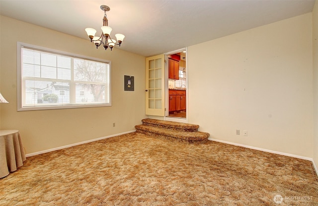 carpeted empty room with baseboards and a chandelier