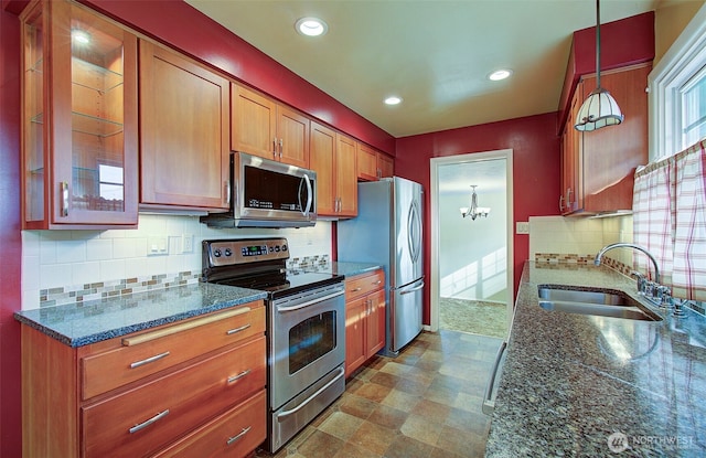 kitchen featuring glass insert cabinets, dark stone countertops, appliances with stainless steel finishes, brown cabinets, and a sink