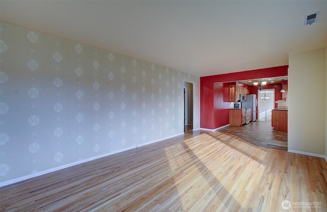 empty room with visible vents, wallpapered walls, baseboards, and wood finished floors