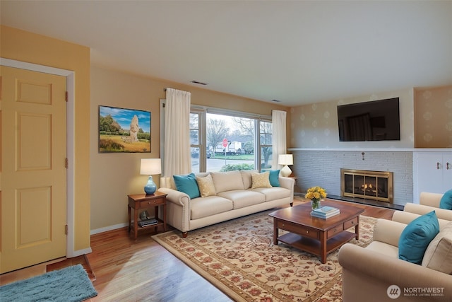 living room with visible vents, light wood-style flooring, a fireplace, and baseboards