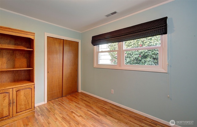 unfurnished bedroom with visible vents, ornamental molding, a closet, light wood finished floors, and baseboards