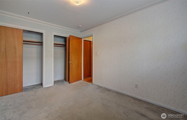 unfurnished bedroom with carpet flooring, baseboards, two closets, and ornamental molding