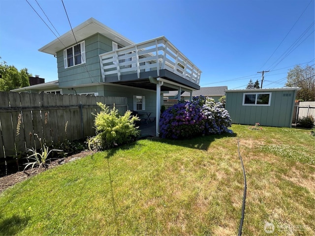 rear view of property featuring an outbuilding, fence, a lawn, and a wooden deck