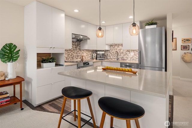 kitchen with a sink, stainless steel appliances, a breakfast bar area, white cabinets, and decorative backsplash